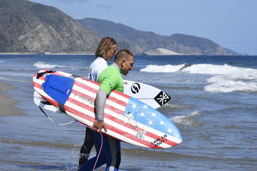 Two men wade into the ocean carrying surfboards.
