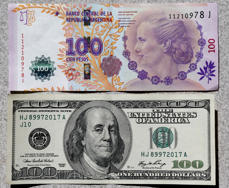 An Argentine 100 pesos bank note (top), featuring an image of former first lady Eva Peron, is displayed next to a U.S. $100 note. At the official rate, $1 is about 8.5 pesos.​ But the so-called blue-dollar rate – which is actually the black market rate — is about 13 pesos to the dollar.