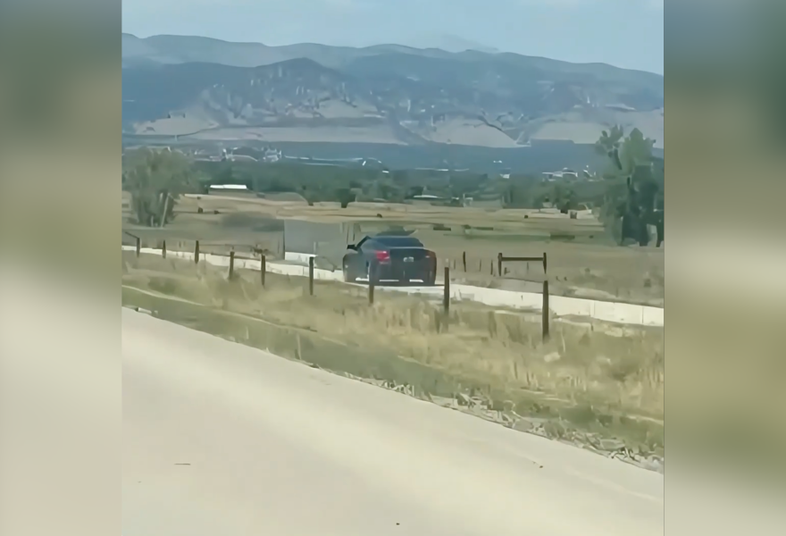 A car driving alongside a road with mountains in the background.