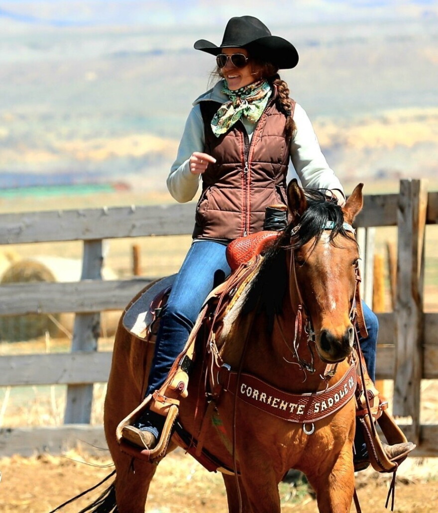 A woman in a black cowgirl hat rides a brown horse.
