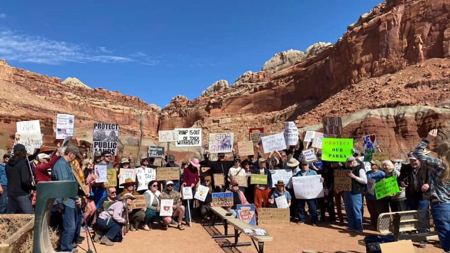 Dozens of people gathered outside red rock mountains holding signs like "Protect our parks!"