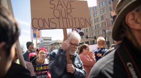 A demonstrator holds a sign reading "Save our Constitution" as he walks through a crowd in Wichita, Kan. on Saturday, March 28, 2026. Demonstrators were escorted and by police throughout the protest.