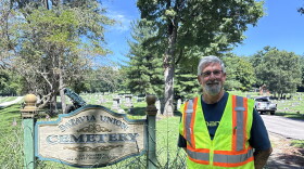 A man in a neon safety vest stands next to a sign that says, "Batavia Union Cemetery."