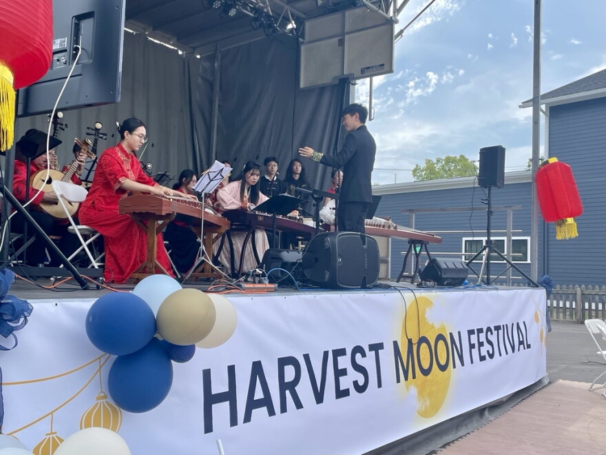 Performers in traditional Chinese dress and playing various traditional instruments sit on stage during the 2024 Harvest Moon Festival at Schoen Place in Pittsford.