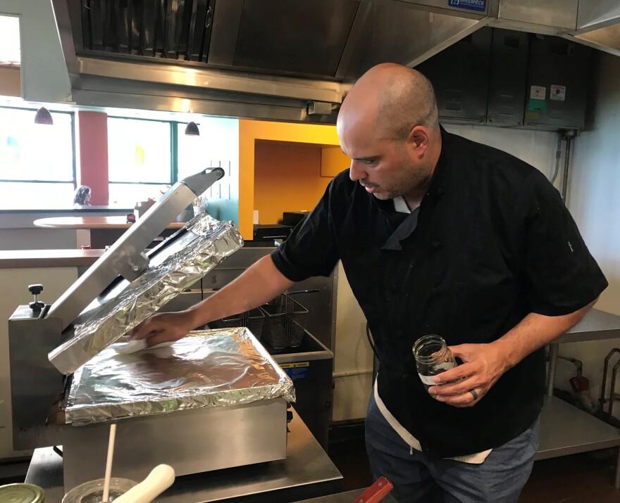 A man in a black shirt wiping down a toasting press.