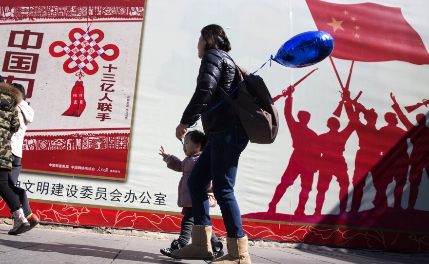 A child walks near government propaganda one of which reads "1.3 billion people united" on the streets of Beijing, China, Tuesday, March 8, 2016.