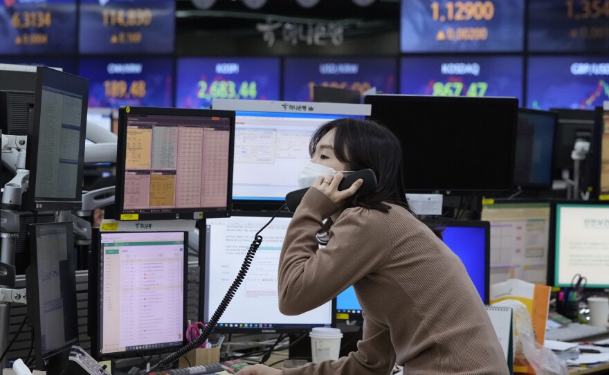 A person in a face mask speaks into a phone while looking at a computer in a room of TV screens. 