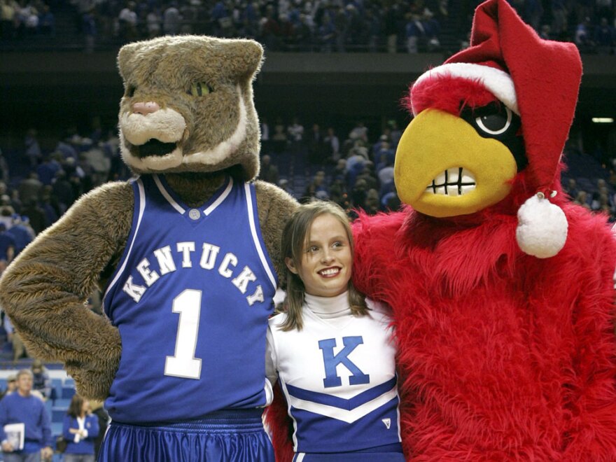 A cheerleader for the Kentucky Wildcats stands between the mascots for Kentucky and the Louisville Cardinals as they sing "My old Kentucky Home" after the game at Rupp Arena on December 17, 2005 in Lexington, Kentucky. In our second hour, die hard fans talk about long standing team rivalries in their town.