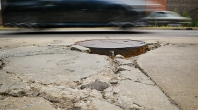 Traffic moves past a crumbling part of Troost Avenue where the pavement is crumbling around a series of sewer maintenance holes Friday afternoon.