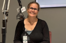 Woman in a lack sweater seated next to a microphone in a radio studio