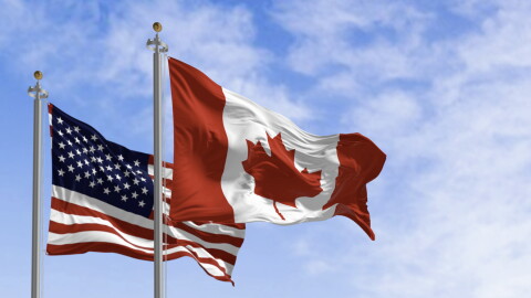 Canada and american national flags waving in the wind on a clear day. 