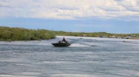 A skiff speeds up a river with low-lyingg bans