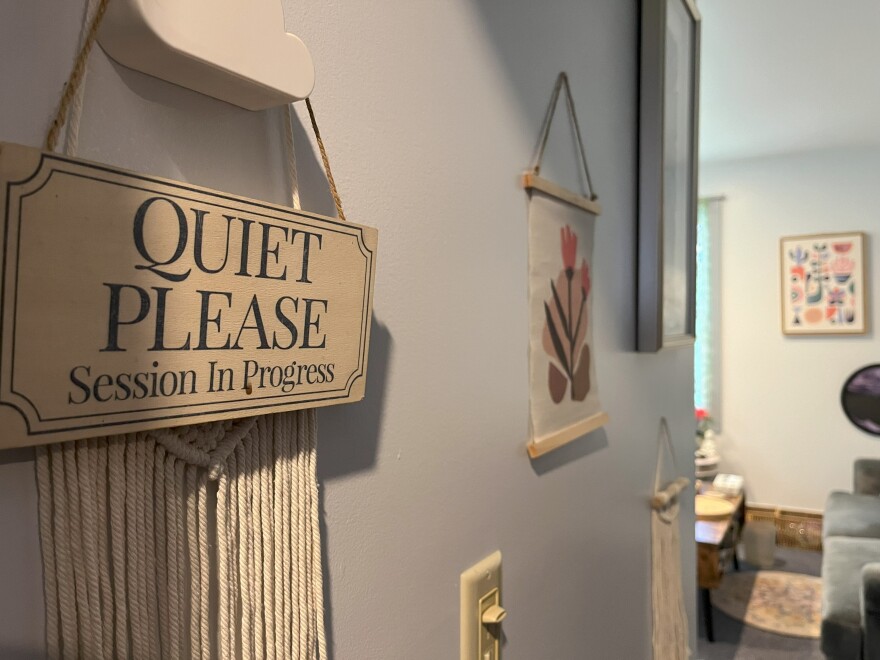 A wooden sign hanging on an office wall says "Quiet please: Session in progress." A therapist's office is visible in the background.