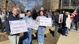 Three young women hold protest signs in Uptown Normal