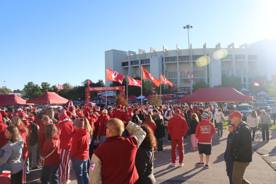 Crowds of people in red and white in the parking lot outside of Memorial Stadium on game day.