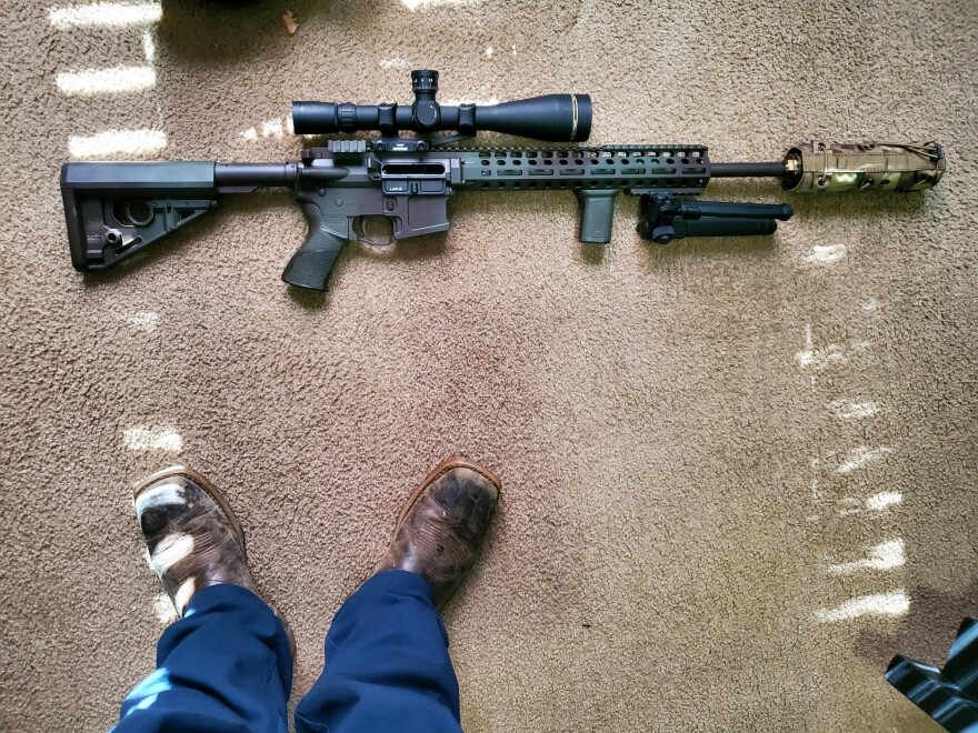 machine gun on the ground with someone's feet standing next to it.