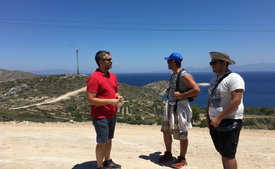Stathis Kontos, who works for the Tilos municipality, talks to two tourists about the clean energy project after they spot the wind turbine in the distance.