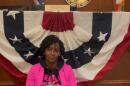 Rep. Angie Nixon sits on the floor in Gov. DeSantis' office entrance, leaning against a wood-paneled desk draped with red, white and blue bunting. She wears a bright pink blazer.