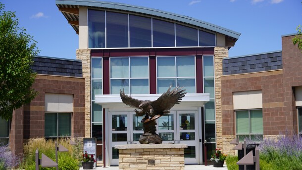 An eagle statue rises before the front doors of a modern building.
