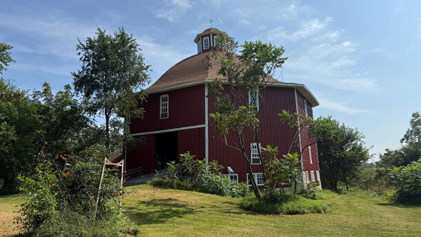 A red, octagonal barn is seen among greenery. 