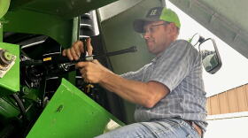 Farmer sits on a tire working on a combine.