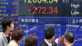 Passersby watch share prices spike in Tokyo on April 4, the day Japan's central bank announced a massive purchase of government bonds. The bank hopes the scale of the effort will boost Japan's slow-moving economy.