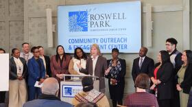Roswell Park Comprehensive Care Center CEO Candace Johnson, standing at microphone, discusses the future impact of the cancer center's expanded community outreach center.
