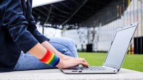 Close-up of a woman's hands using a laptop and wearing a rainbow wristband at a park.