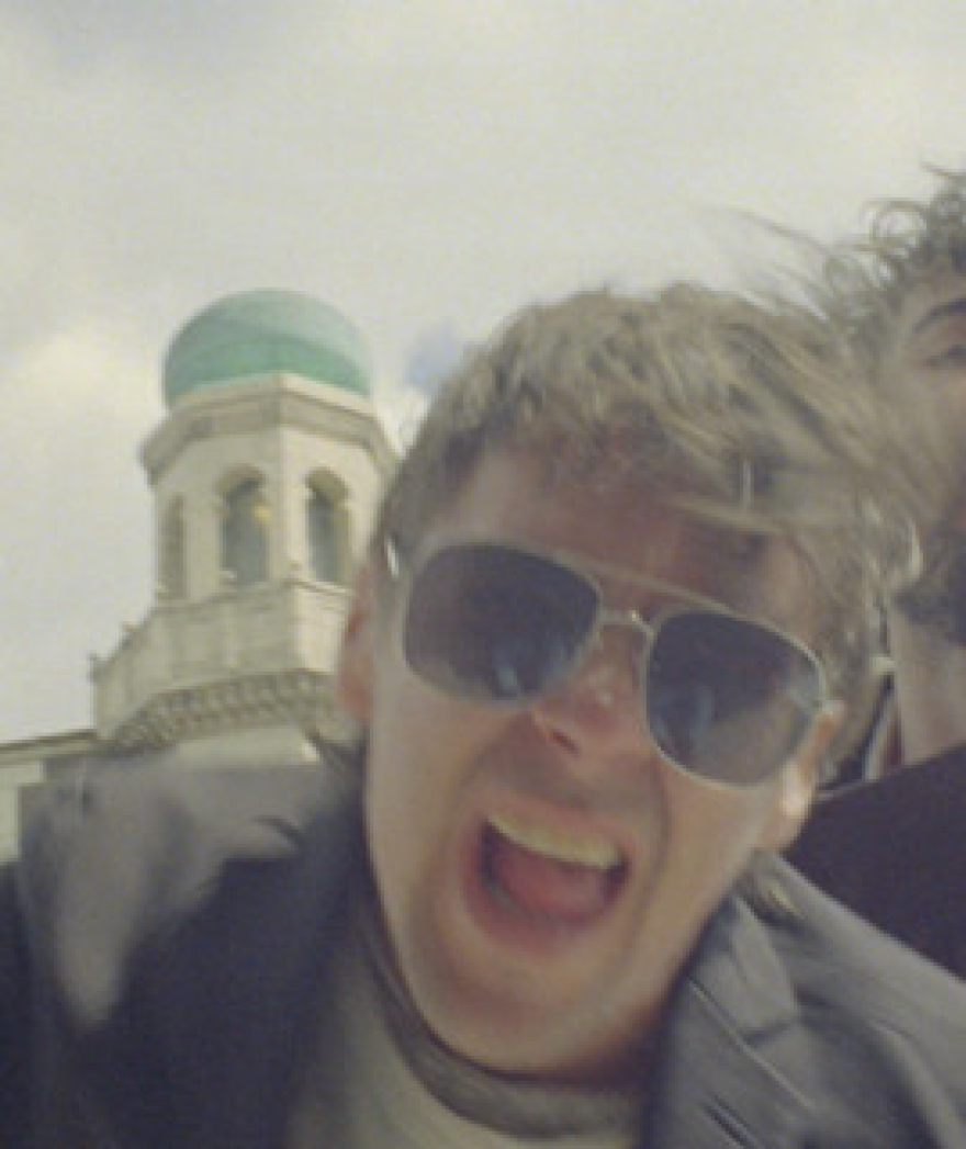 A man wearing sunglasses, facing forward with his mouth open as if singing