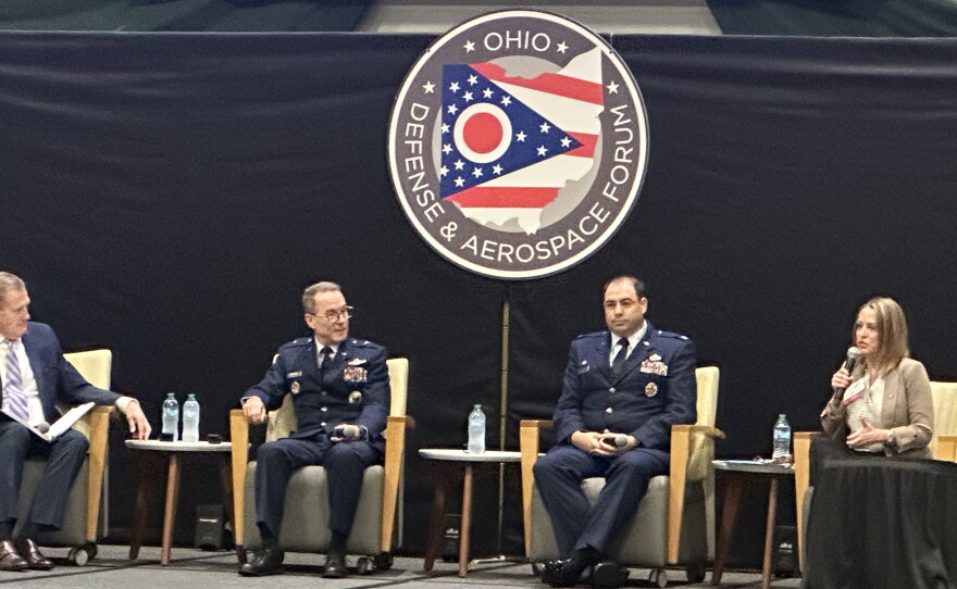 Three men and a woman sit in chairs on a stage below an an Ohio Defense & Aerospace Forum sign.