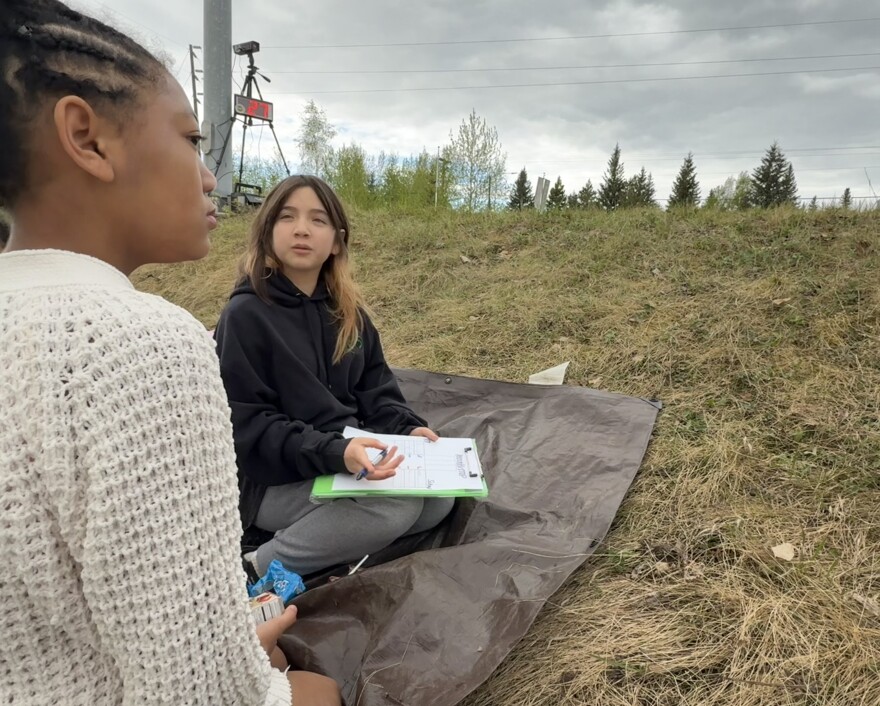 Sixth-graders Nailah Phillips, left, and Isabella Vang, right, who attend Tanana Middle School in Fairbanks, watch traffic from a ditch near the corner of Trainor Gate Road and F Street May 26, 2026.