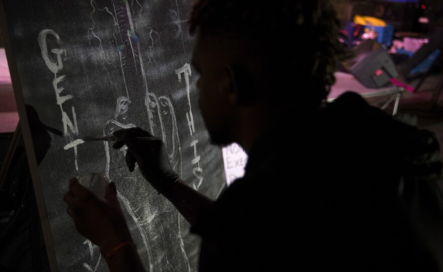 Artist Joseph Francis paints a sky scraper as a middle finger with the words 'Gentrify This,' during a rally on Wednesday, November 1, 2017, outside of City Hall in Seattle. 