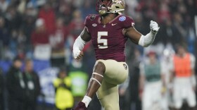 Football player walks with one hand in the air and one leg raised high.