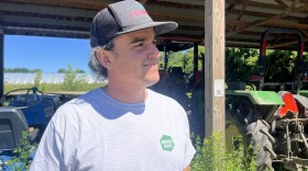 A white man with a baseball hat stands in front of a tractor.
