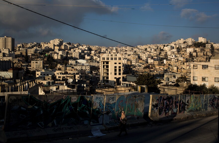 A Palestinian woman walks earlier this month past a concrete barricade on the road that separates an Israeli settlement and a Palestinian neighborhood in Hebron.