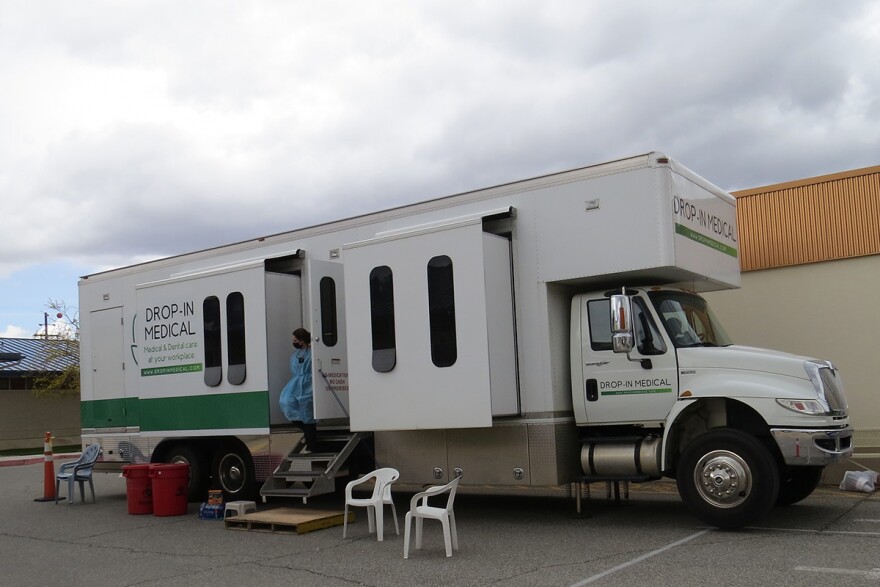 A white truck is parked in a parking lot, with its door propped open and chairs are set up outside. A woman steps down from the van. 