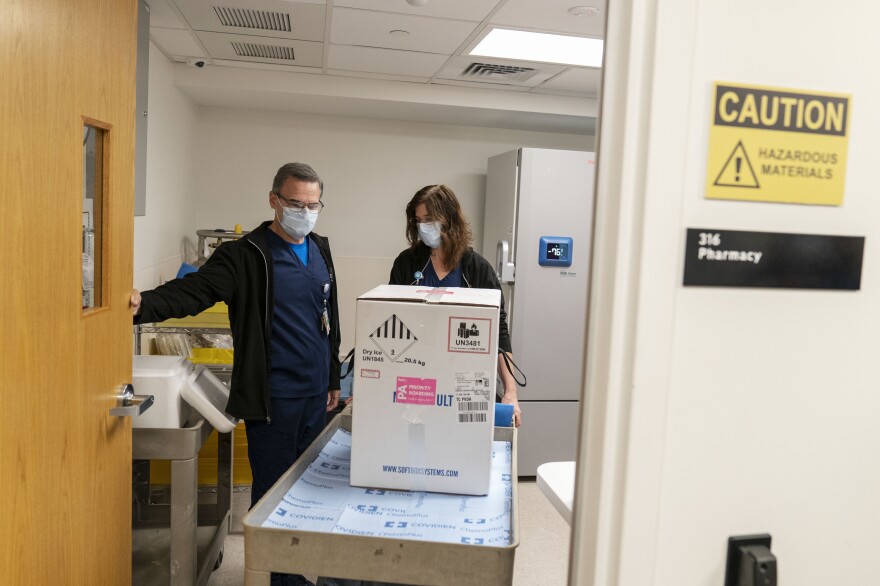 Pharmacists Richard Emery, (left) and Karen Nolan, wheel a box containing the Pfizer-BioNTech COVID-19 vaccine next to a storage freezer as it arrives at Rhode Island Hospital in Providence, R.I, on Monday.
