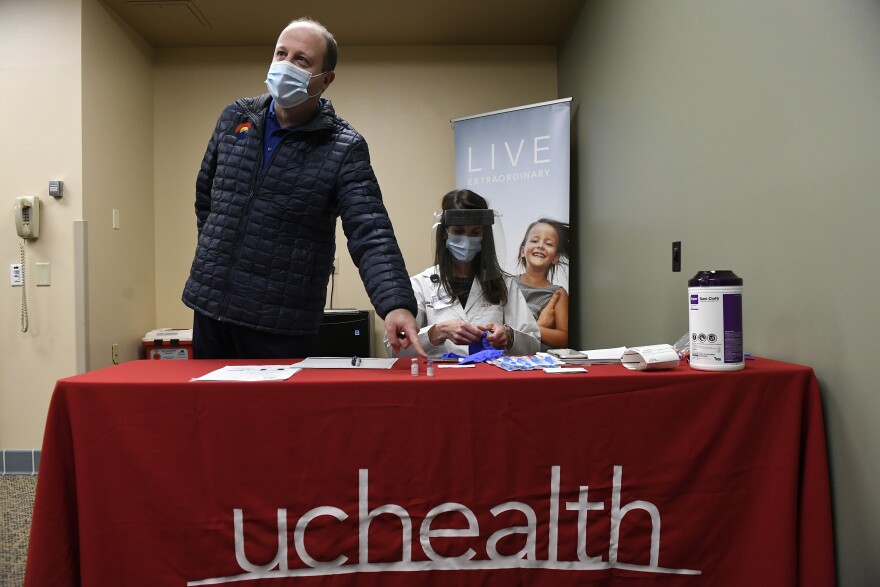 FORT COLLINS, COLORADO - NOVEMBER 14: Colorado Governor Jared Polis, left, points to the Covid-19 vaccine in a small vial as he watches as Gina Harper, clinical coordinator with pharmacy, right, reconstitutes a dose of the Covid-19 vaccine before it is administered to the first patients in Colorado at UC Health Poudre Valley Hospital on December 14, 2020 in Fort Collins, Colorado. The first Covid-19 vaccines were administered in Colorado to frontline health care workers in Fort Collins and Colorado Springs today. Governor Jared Polis joined these nurses, doctors, respiratory therapists and other frontline workers in the cafeteria of hospital as one by one they got the vaccine. A total of twenty vaccines were administered to twenty doctors, nurses, respiratory therapists and others from Northern Colorado medical facilities. During the process of preparing the vaccines, Harper adds sodium chloride to reconstitute the vaccine before injecting it into patients. Governor Jared Polis said that today's event shows the triumph of modern science and that the end of the pandemic is in sight. (Photo by Helen H. Richardson/The Denver Post, Pool)