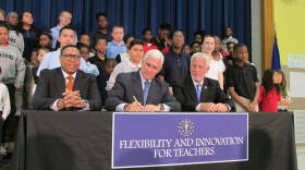 Pence signs House Bill 1009 while IPS Superintendent Lewis Ferebee (left) and Indiana House Education Committee Chairman Robert Behning, R-Indianapolis, and School 88 students look on.