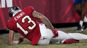 Football player wearing a red 13 jersey on the ground holding his hamstring