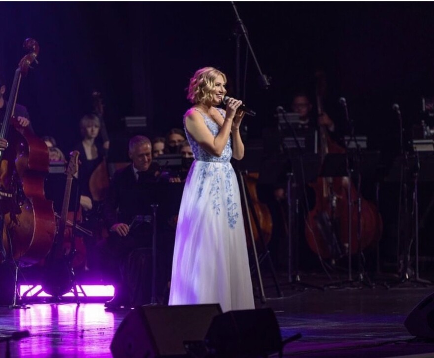 A womanin a white dress stands at a mic onstage.