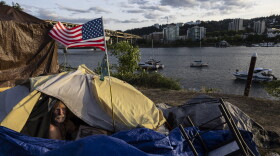 FILE - Frank, a homeless man, sits in his tent with a river view, June 5, 2021, in Portland, Ore. Momentum is building in a case regarding homeless encampments before the U.S. Supreme Court that could have major implications for cities as homelessness nationwide has reached record highs. (AP Photo/Paula Bronstein, File)