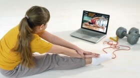 A young girl following a gym routine on a laptop.