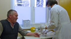 A doctor takes a blood sample from an older patient.