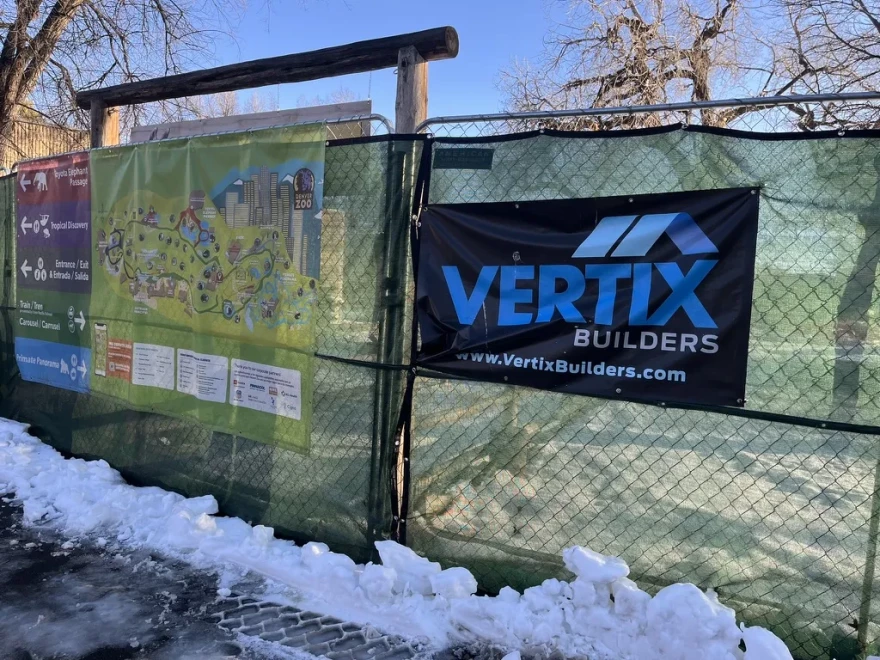 A green chain link fence at the Denver Zoo bears a map of the zoo and a sign for Vertix Builders. 