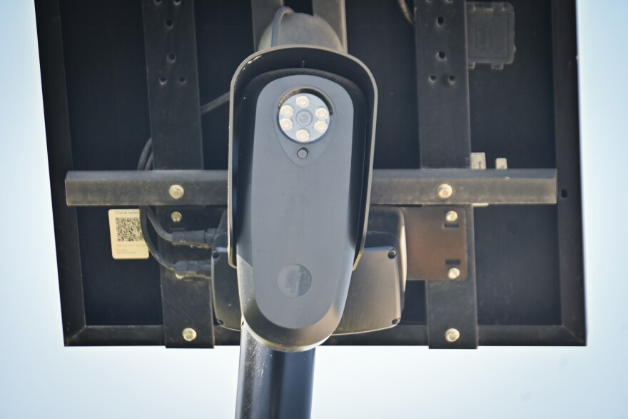 Outdoor, close-up photo of a small black camera attached to a small solar panel.
