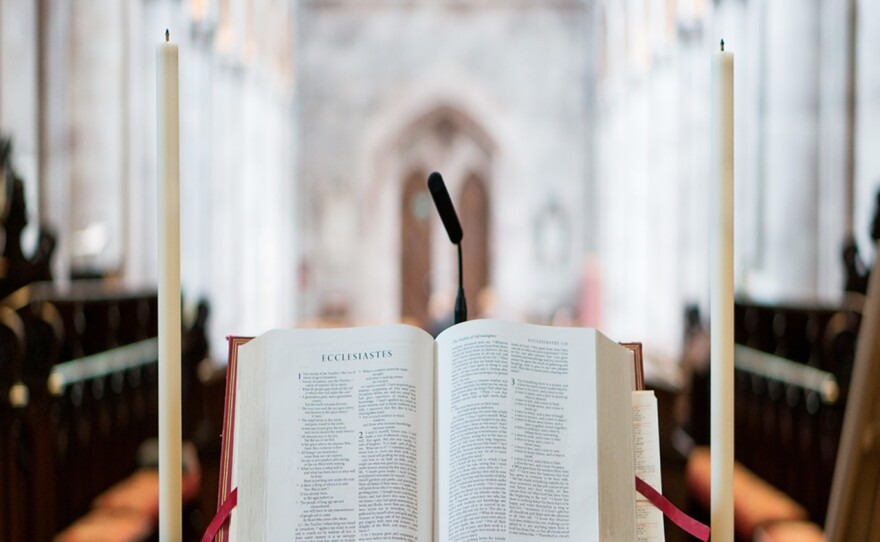 a bible rests on a stand flanked by two tall candles. pews are in the blurred background
