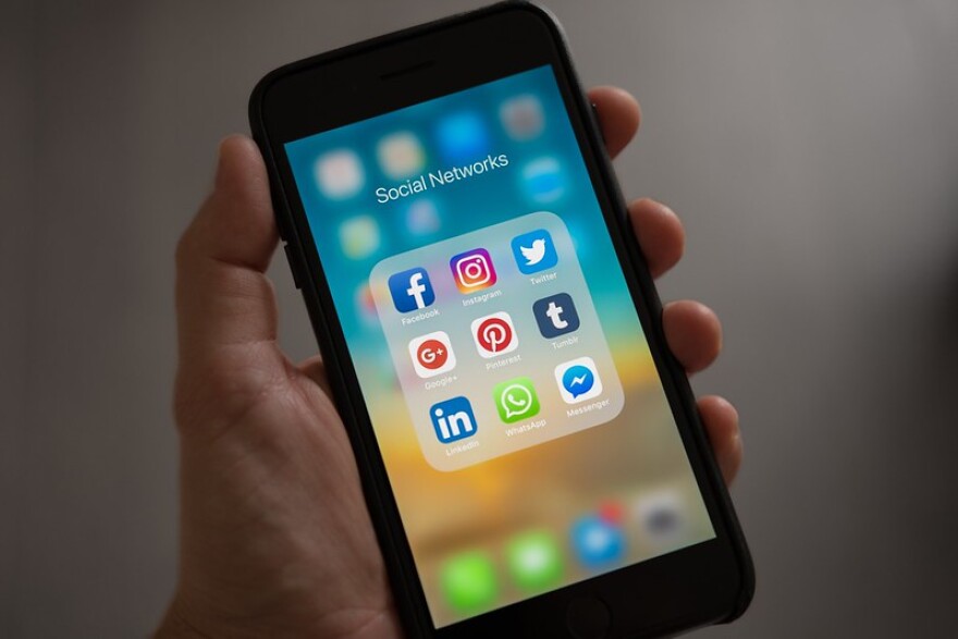 A hand is holding a cell phone. On the screen, there are social media app icons on display.