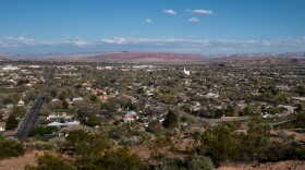  The city of St. George, seen from above. A grid of rooftops, treetops stretch out towards red cliffs in the distance. 