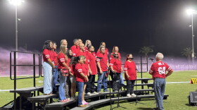 Community members sing the national anthem during the Kerman High School football homecoming game.